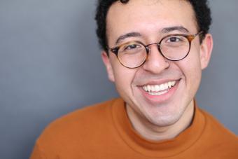 Mateo Hernandez smiles, wearing glasses and an orange shirt