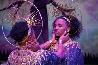 Two boys in mystical robes and halo hold each other's faces and tare into each other's eyes