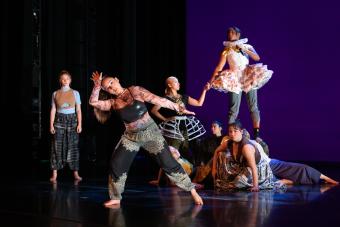 A group of dancers in Renaissance-esque costumes pose on stage