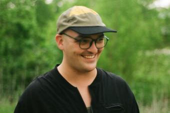Headshot for Daphne Silbiger, a playwright and MacDowell Fellow, wearing a hat, a black shirt and glasses and smiling