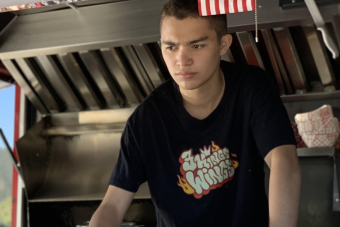 A person wearing a black t shirt looks serious in a kitchen