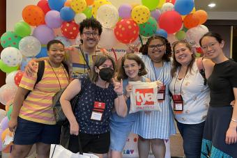 Faculty member Sara Simons and six UT grad students pose together in front of a colorful balloon arch at TYA/USA