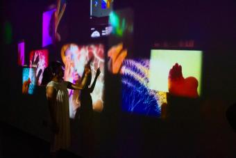 A viewer interacting with projected images on a wall, which are colorful and layered over each other