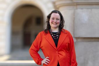 Course instructor Amira Pollock poses in a red blazer in front of an academic building.