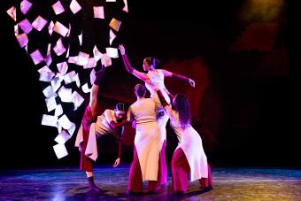 Dancers lift another dancer above their heads in To Offer A Withheld Embrace. A dancer to the side of the group gazes at the lifted dancer as they lift their leg to their face, leaning of the base of the lift with their left arm.