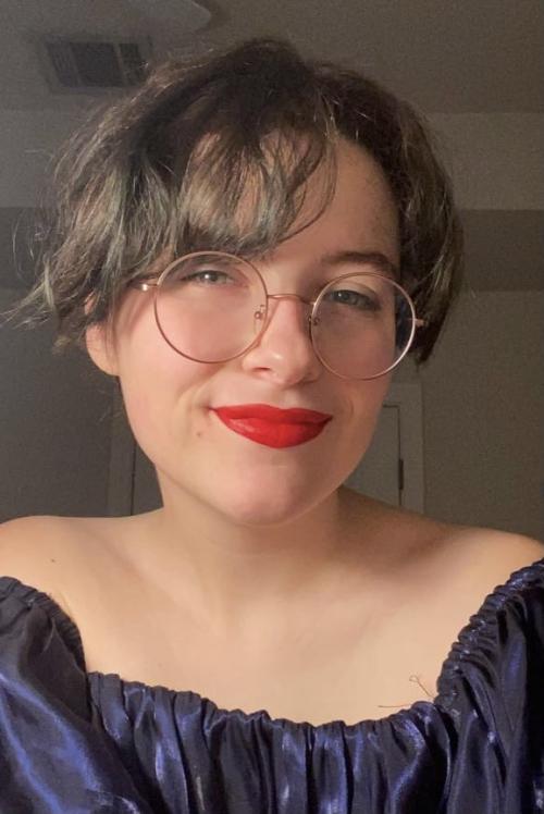 woman with short brown hair wearing round glasses and red lipstick