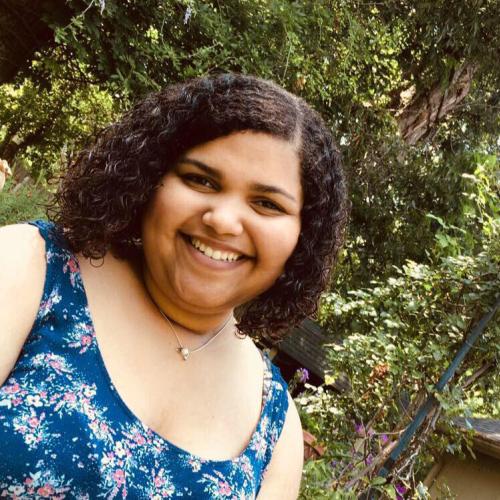 woman with short, curly hair smiling and standing in front of trees