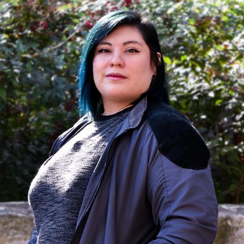 headshot of a woman with turquoise hair standing in front of greenery