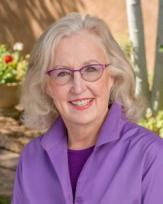 woman with long silver hear wearing purple rimmed glasses and a purple shirt