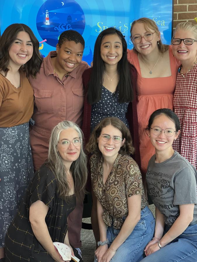 group photo of eight collaborators posing in front of a banner for SPELLS OF THE SEA