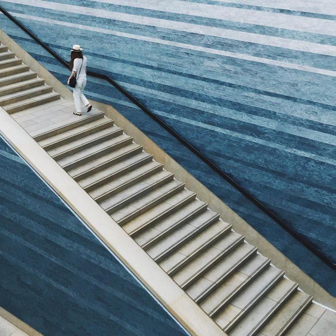 person walking up stairs with the art piece STACKED WATERS next to them